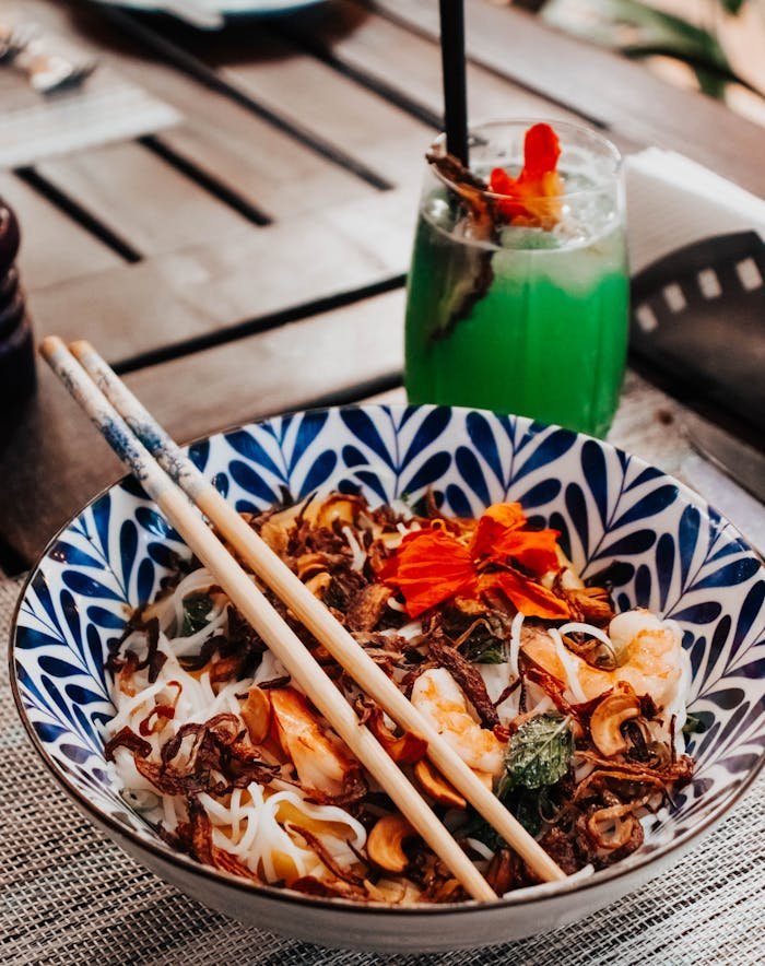 Colorful noodle dish paired with a refreshing green cocktail, set outdoors in Nairobi, Kenya.